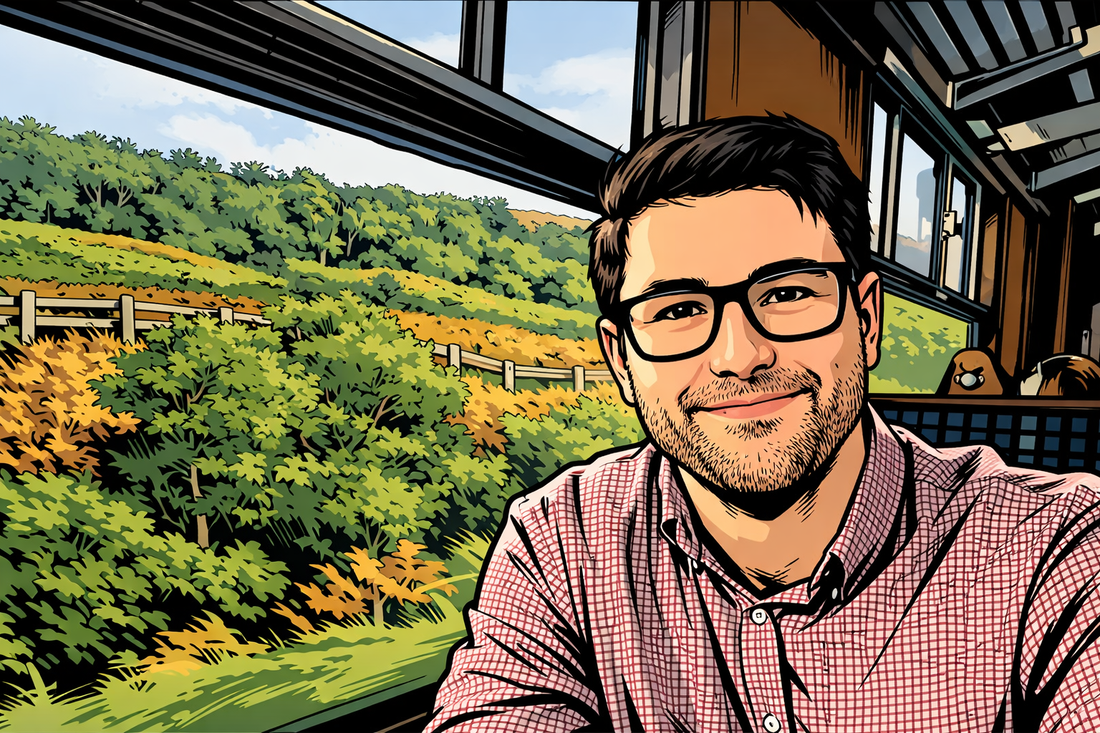 Man with glasses sitting on a train looking out at a scenic view of greenery.
